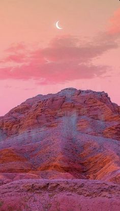 the moon is setting on top of a mountain in the desert, with pink clouds