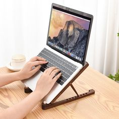 a person using a laptop on a wooden table with a cup and saucer next to it