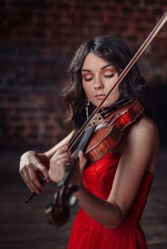 a woman in a red dress holding a violin and looking down at the bow she is wearing