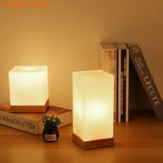 two lit candles sitting on top of a wooden table next to books and a plant