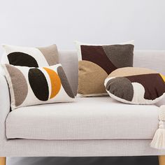 a white couch with four pillows on it and a tasseled pillow in the middle