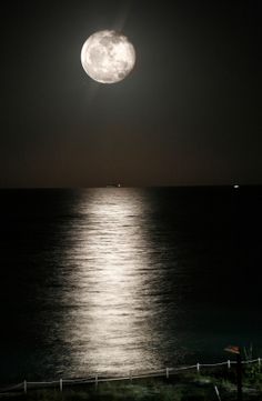 the full moon is shining over the ocean