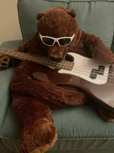 a teddy bear is sitting on a couch with a bass guitar in its lap and wearing sunglasses