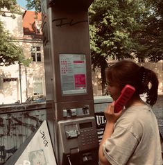 a woman standing next to a parking meter talking on a red phone