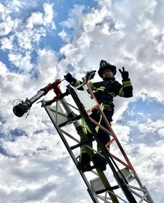 a fireman standing on top of a ladder next to a radio tower under a cloudy blue sky