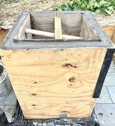 a wooden box sitting on top of a sidewalk next to a trash can and bucket