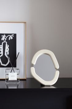 a white sculpture sitting on top of a black table next to a glass vase and mirror