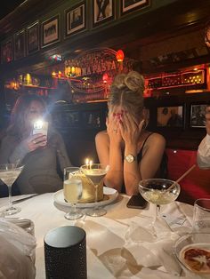 two women sitting at a table with drinks and cell phones in front of their faces