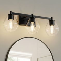 a bathroom vanity light with three bulbs on the side and a round mirror above it