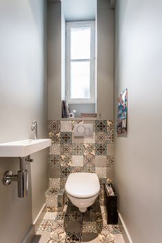 a toilet and sink in a small room with tile flooring on the walls, along with a window