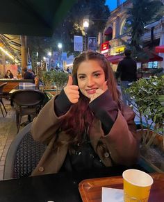 a woman sitting at a table giving the thumbs up