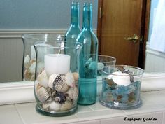 some glass bottles are sitting on a counter with seashells and candles in them