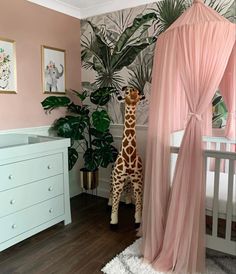 a giraffe standing next to a baby crib in a room with pink walls