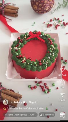 a christmas cake in a box decorated with green and red icing, surrounded by cinnamon sticks