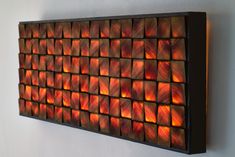 a wall mounted art piece on the side of a white wall with red and orange squares