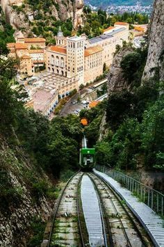 a train traveling down tracks next to a lush green forest covered hillside with buildings on both sides