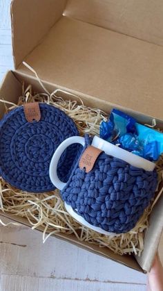 a blue crocheted coffee cup and saucer in a cardboard box