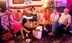 a group of people sitting around a table in a living room next to a christmas tree