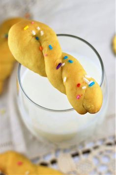 two doughnuts on a stick with sprinkles next to a glass of milk