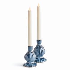 two blue candles sitting next to each other on top of a white surface with one candle in the middle