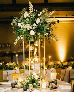 a tall centerpiece with white flowers and greenery sits on top of a round table