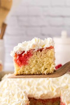 a piece of cake with white frosting and strawberries on top is being lifted by a wooden spatula