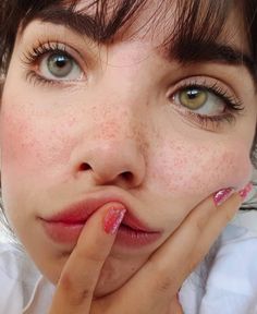 a close up of a person with freckles on her face and hand near her mouth