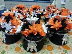 several black and orange flower pots sitting on top of a table covered in paper flowers