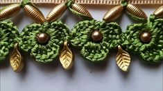 three green crocheted flowers with gold leaves and pearls on each side, along with two brown beads