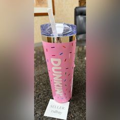 a pink tumbler cup sitting on top of a counter next to a sign that says dunkin'donuts