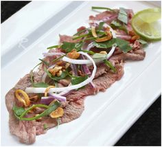 a white plate topped with meat and veggies next to a slice of lime