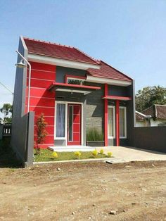 a red and gray house with a black fence around it's perimeter, in the middle of a dirt lot