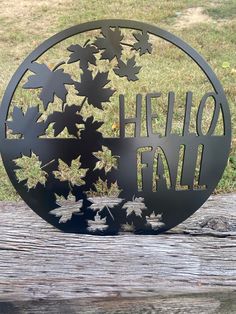 a metal sign that says hello fall with leaves in the center on a wooden table