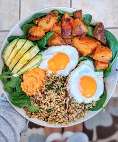 a person holding a bowl filled with rice, eggs and spinach on top of it