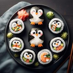 sushi with penguins, carrots and avocado on a black plate next to chopsticks