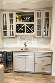 a kitchen with white cabinets and marble counter tops, wine rack on the wall above the sink