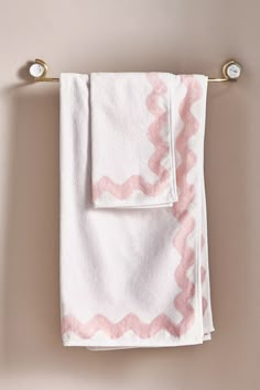 two towels hanging on a towel rack in front of a beige wall with pink and white designs