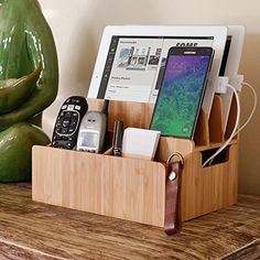 a cell phone and other items in a wooden holder on a table next to a green vase