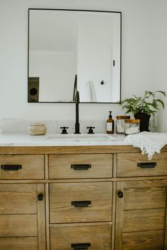 a bathroom vanity with two sinks and a large mirror above it, in front of a potted plant