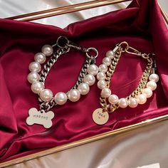 two bracelets with dog tags and pearls in a gold box on a red satin