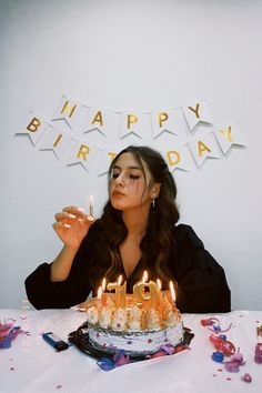 a woman sitting in front of a birthday cake with lit candles on top of it