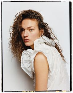 a young woman with curly hair posing for a photo in front of a white wall