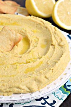 a white plate topped with hummus next to sliced lemons