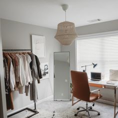 a room with a chair, desk and hanging clothes