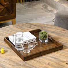 a wooden tray with glasses and a book on it sitting on top of a table