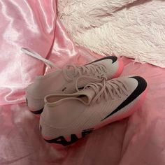 a pair of white and black sneakers on a pink bed sheet with the shoe laces down