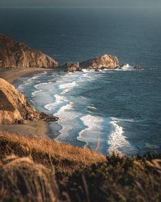 an ocean view from the top of a hill with waves crashing on it's shore