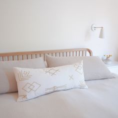 a white bed with two pillows and a lamp on the wall behind it in a bedroom