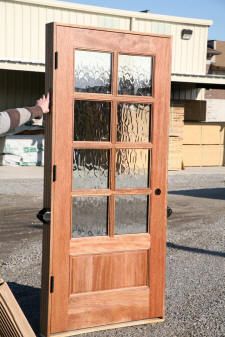 a man standing next to a tall wooden door with glass panels on the front and side