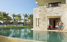 a man and woman standing in front of a pool next to an ocean side resort